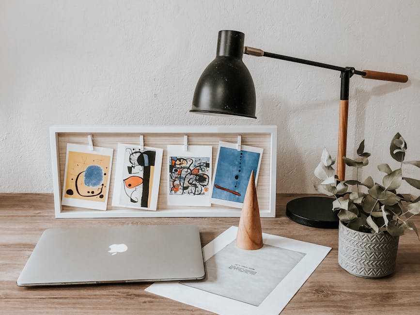 Cozy workspace featuring art prints, laptop, lamp, and plant on desk, perfect for inspiration.