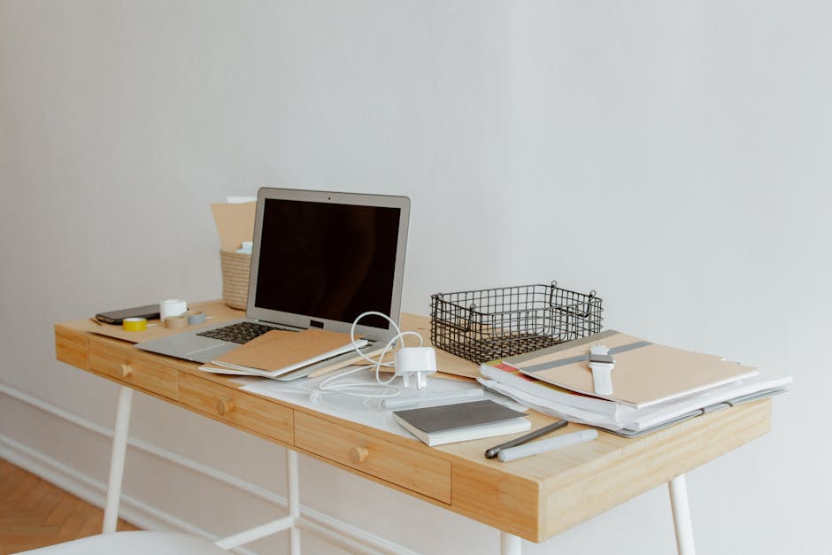 A neatly organized desk with a laptop, notebooks, and office supplies in a minimalist office setting.