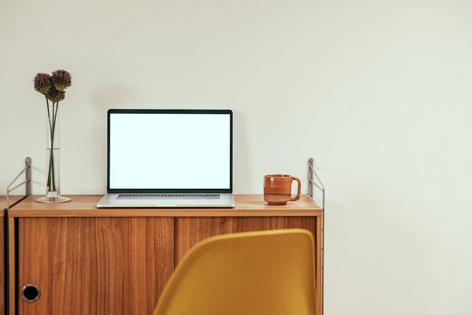 A clean and modern home office desk with a laptop, mug, and vase, emphasizing simplicity and functionality.