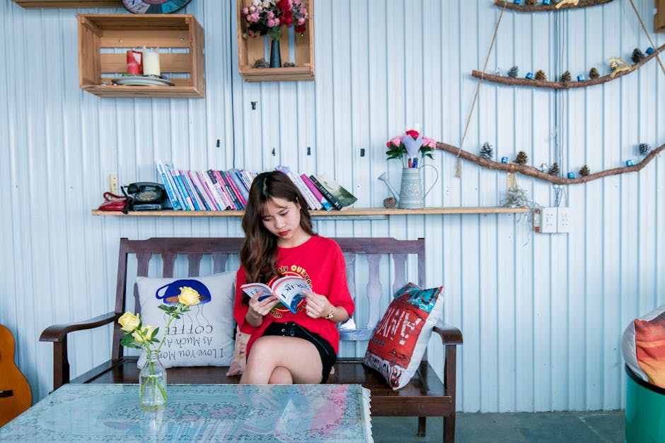 Young Asian woman relaxing indoors while reading a book. Cozy, colorful room for leisure.