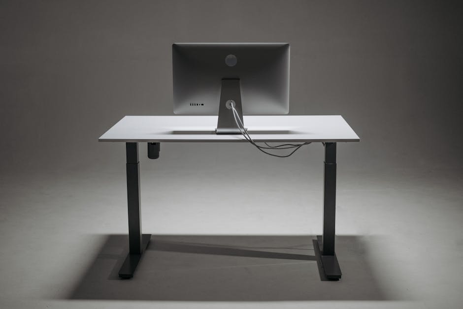 Rear view of a modern height adjustable standing desk with monitor and cable management.