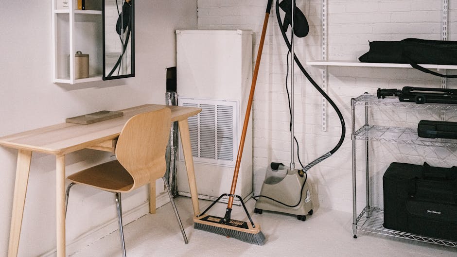 A tidy home office space featuring a wooden desk, chair, broom, and cleaning equipment.