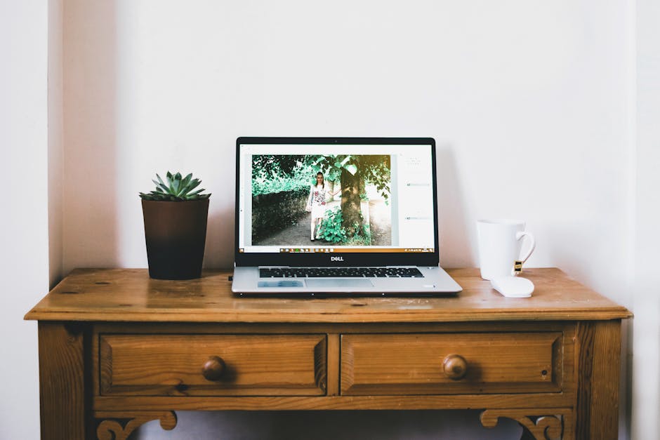 A minimalistic home office setup featuring a laptop, plant, and coffee mug on a wooden desk.