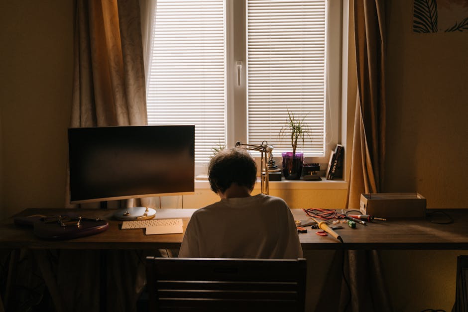 A young man focuses on his electronics hobby, soldering components at a well-organized home desk.
