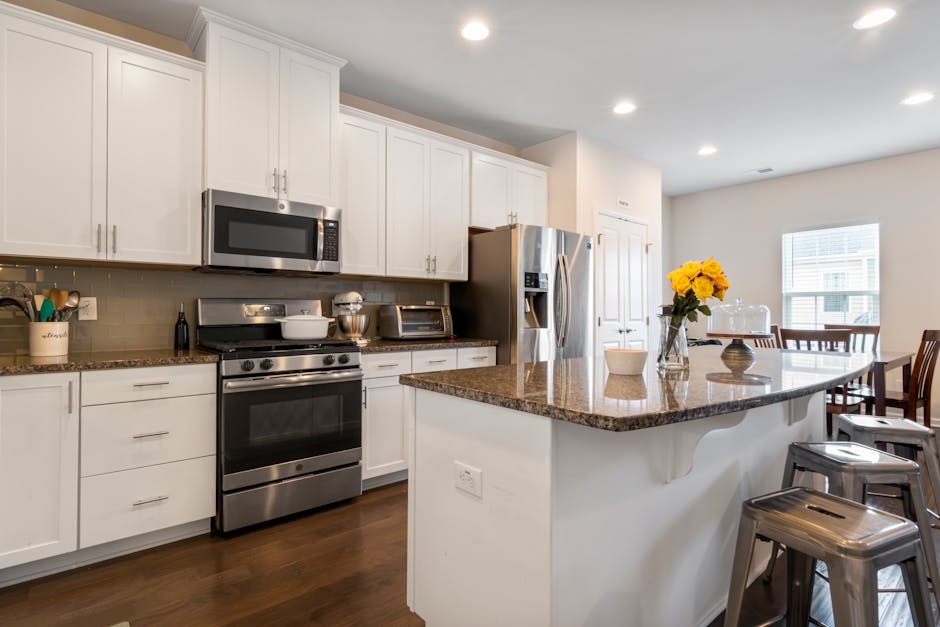 Stylish modern kitchen featuring a central island, stainless steel appliances, and white cabinetry.