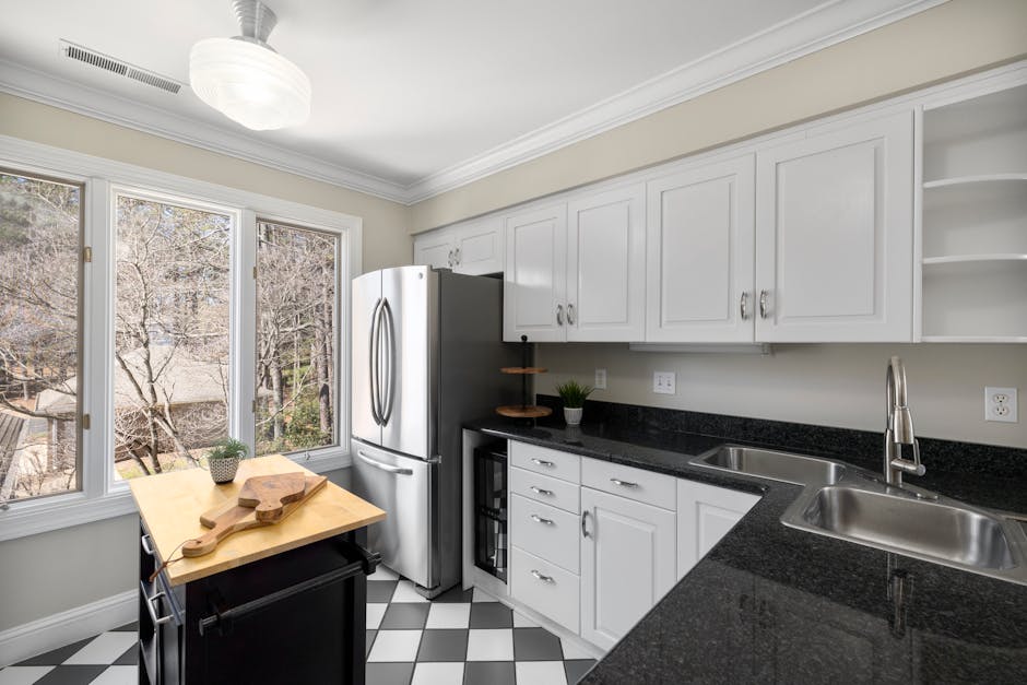Bright kitchen interior with white cabinets, black granite counters, and stainless steel appliances.