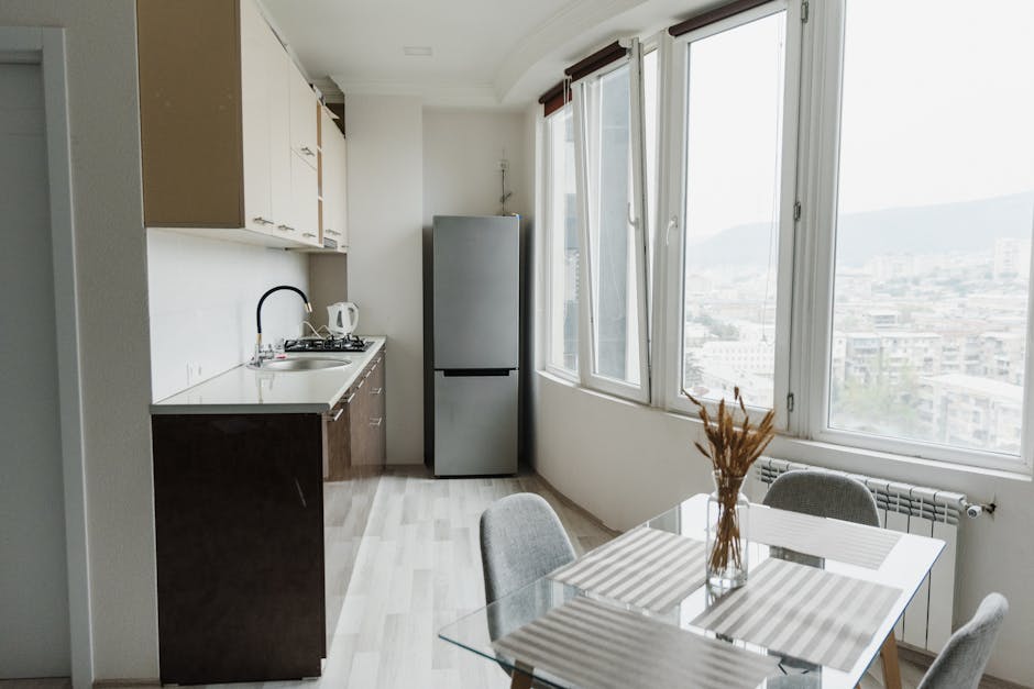Bright modern kitchen with a glass table, minimalist design, and cityscape view through large windows.