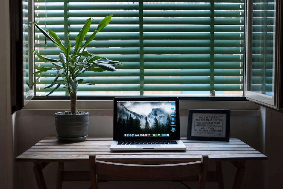 Elegant home office desk setup with a laptop and a plant near a window. Ideal for remote work.