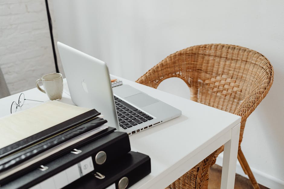 A cozy home office setup featuring a laptop, binders, and wicker chair for productive remote work.