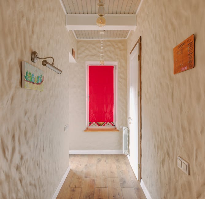A cozy hallway featuring textured walls and a vibrant red window shade.