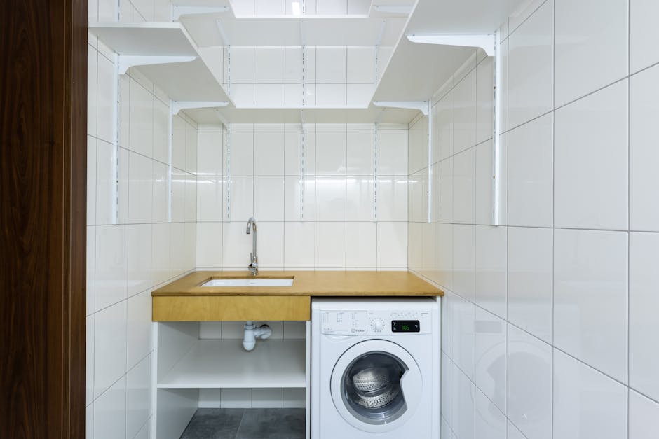 Modern laundry area with white tiled walls, washing machine, and built-in shelves.