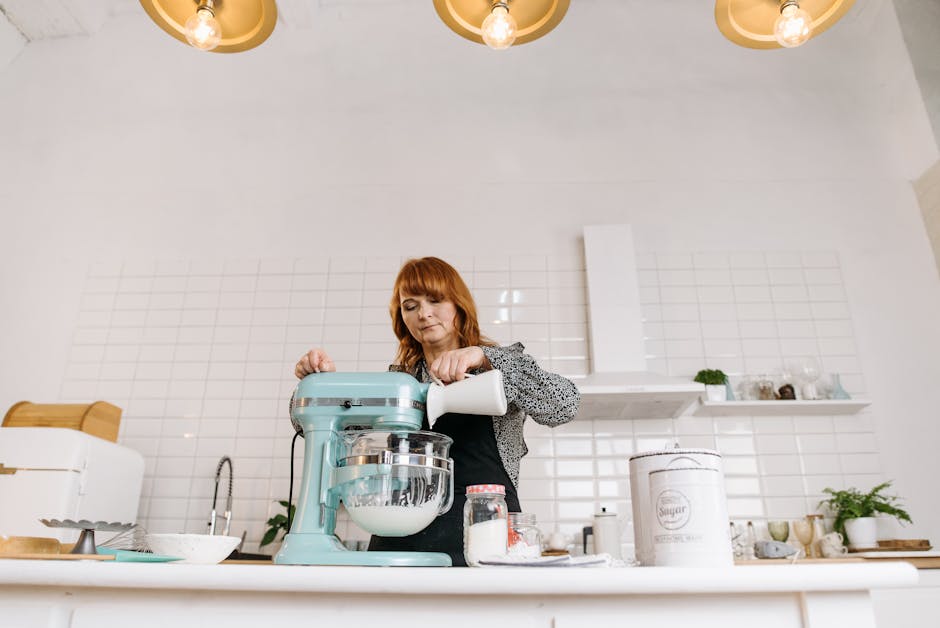 Woman pouring milk into a stand mixer while baking in a stylish kitchen.