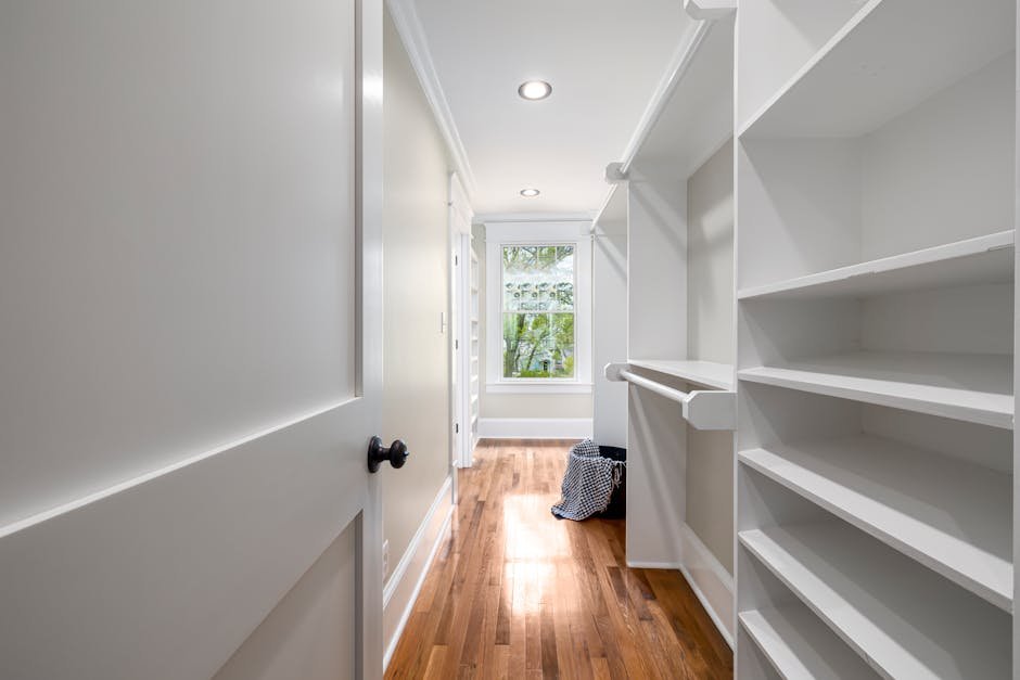 Bright, modern walk-in closet featuring white shelves and wooden flooring. Ideal for home interiors.