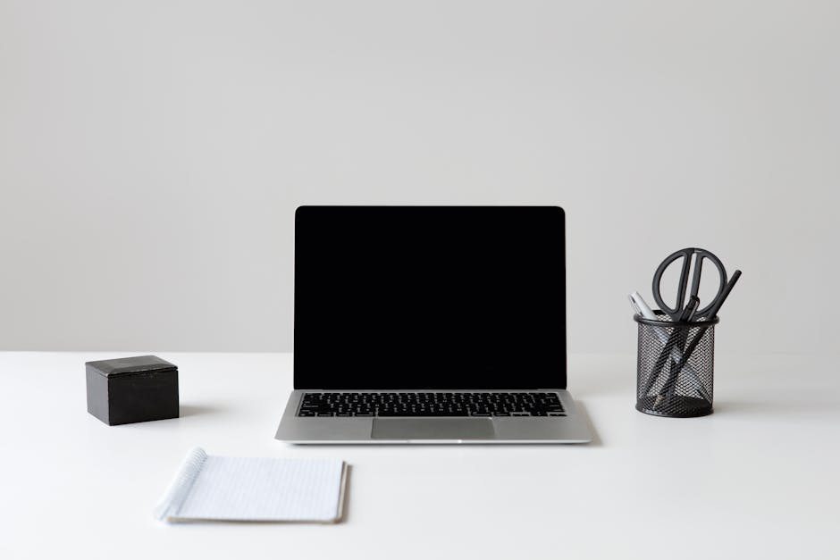 Modern minimalist workspace featuring a laptop, notebook, and stationery on a white surface.