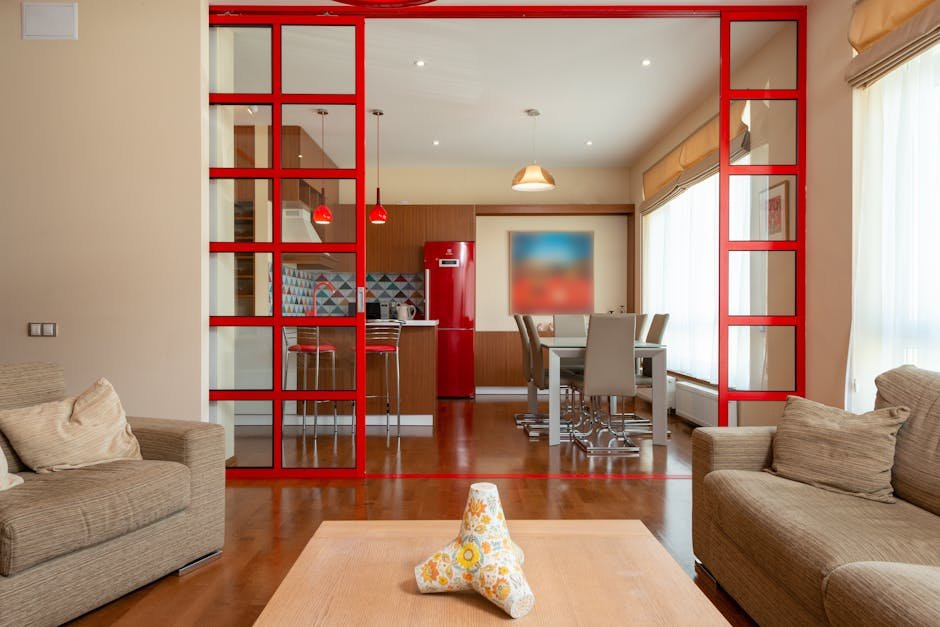 Spacious kitchen area with bright red fridge and dining table placed near living room with comfortable sofa and armchair in modern apartment