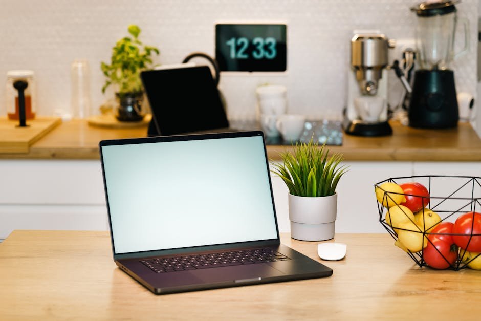A modern kitchen workspace featuring a laptop, coffee machine, and fruit basket, ideal for remote work.